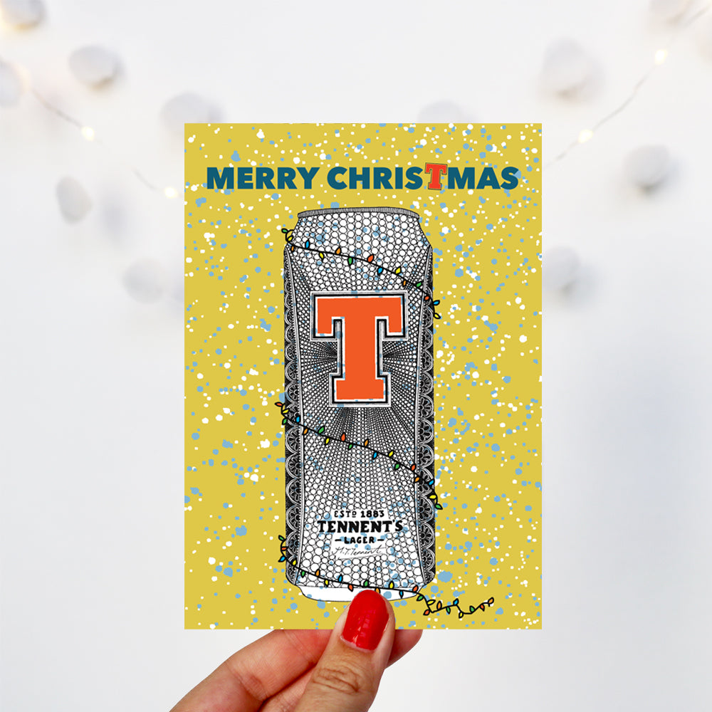 can of tennents wrapped in Christmas lights on a bright card